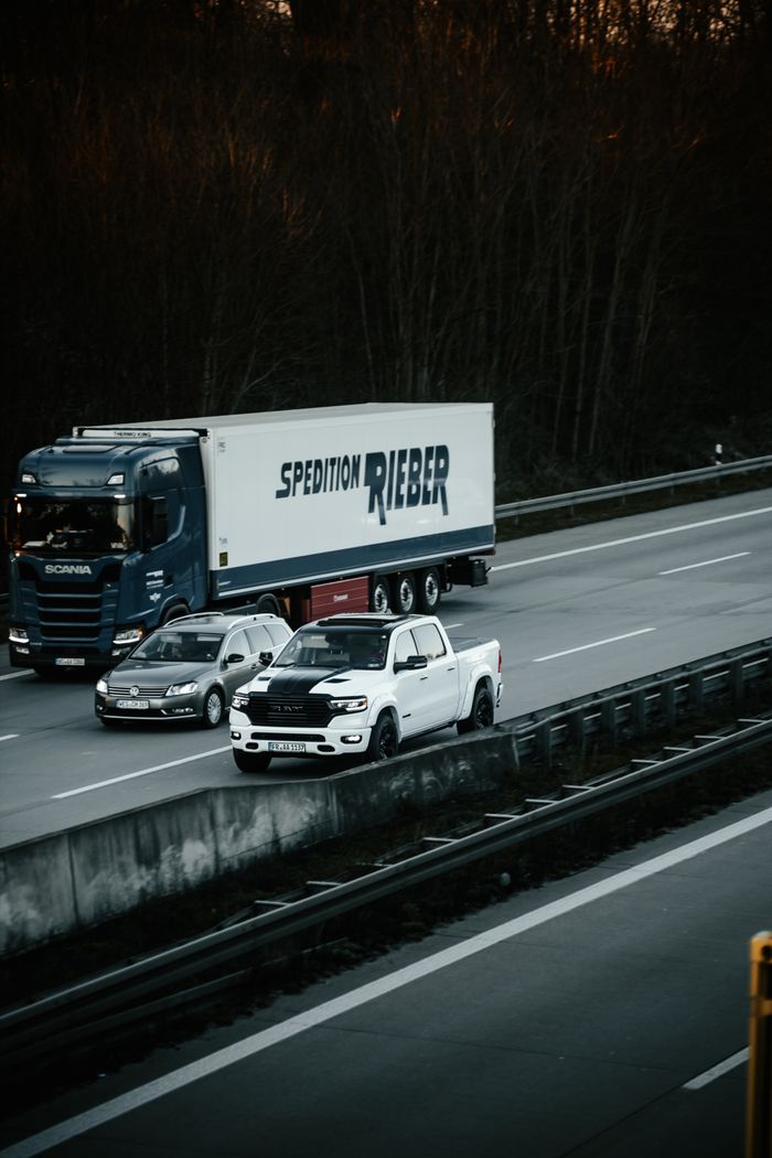 Dodge Ram 1500 and Scania truck on a busy highway at dusk.